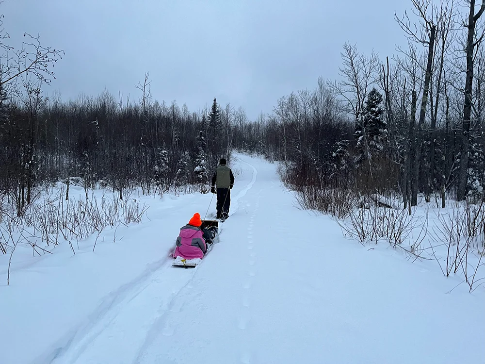 Ely, MN - Dad pulling daugher on homemade pulk sled in winter snow
